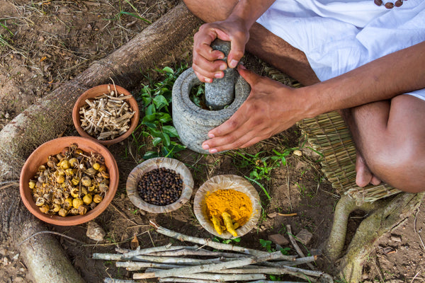 Man grinding herbs in a mortar and pestle. Turmeric, black pepper, ginger roots, and flowers.